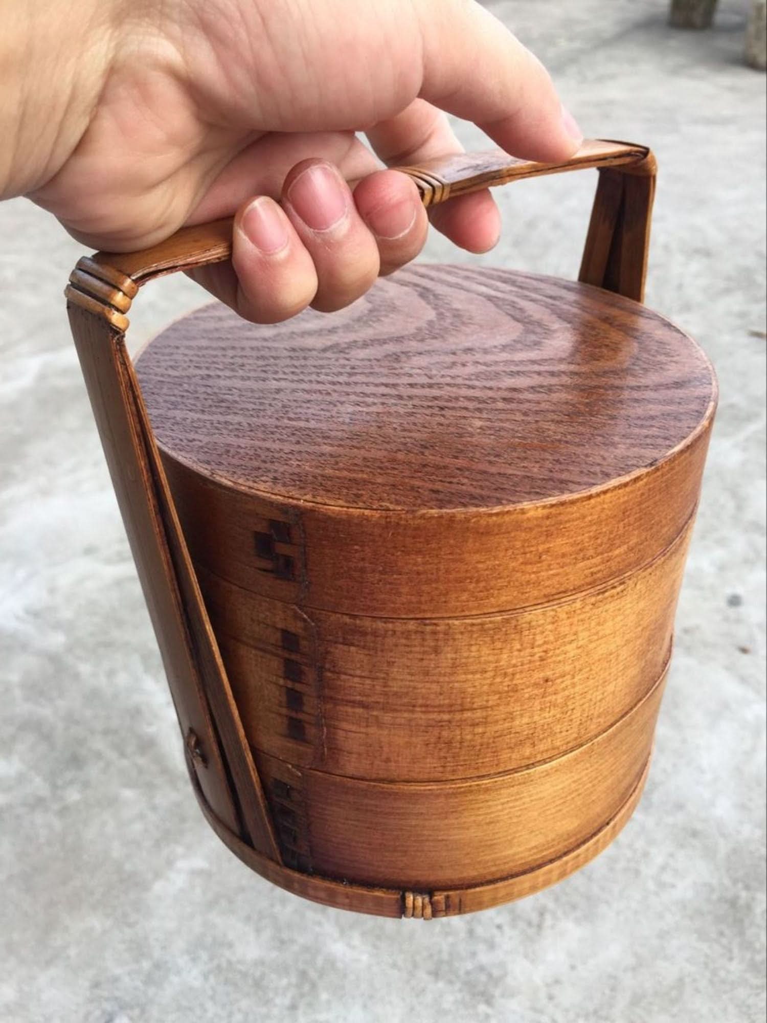 Natural wood Japanese lunch box with a handle, held by a hand.
