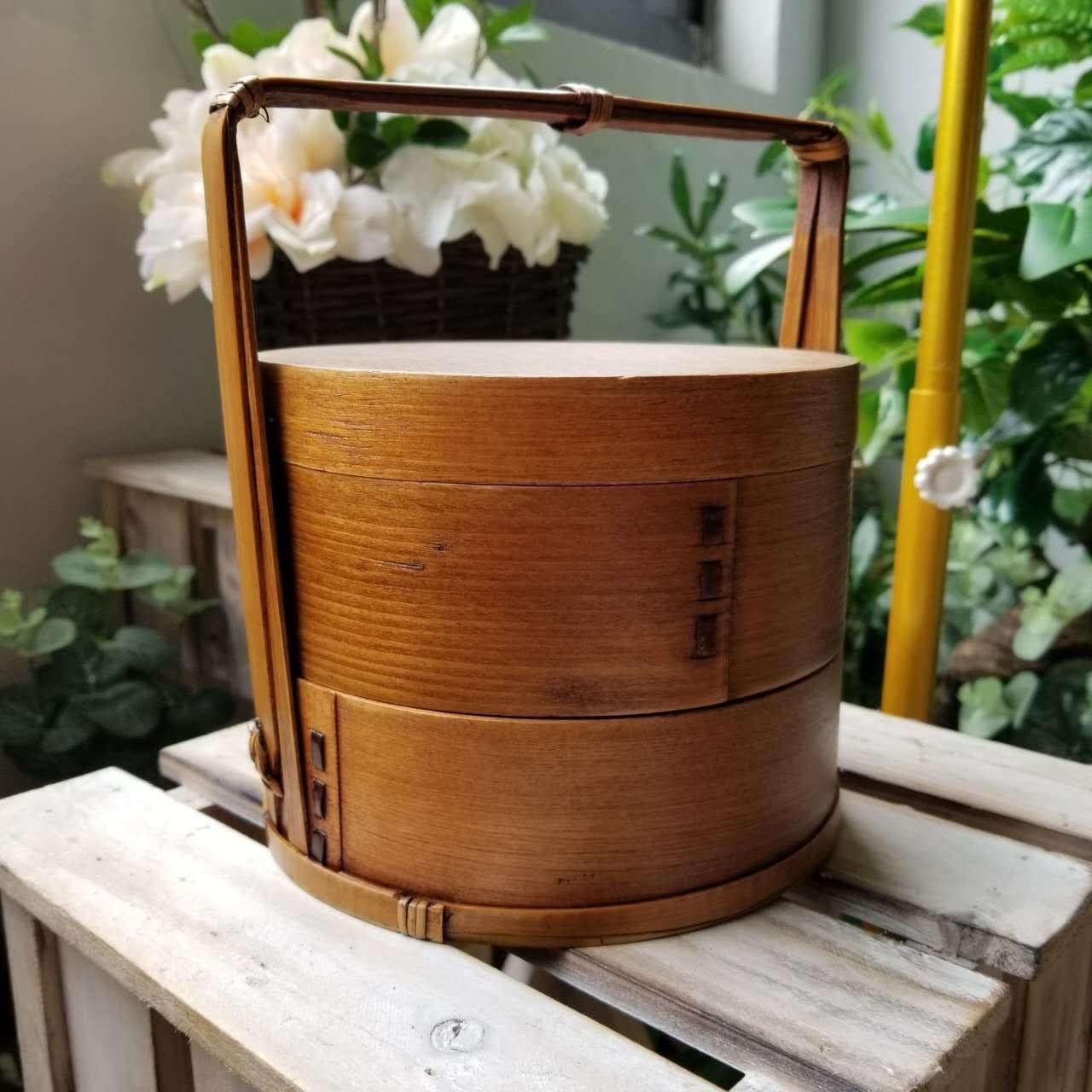 Natural wood Japanese lunch box with bamboo handle on rustic crates, floral background.