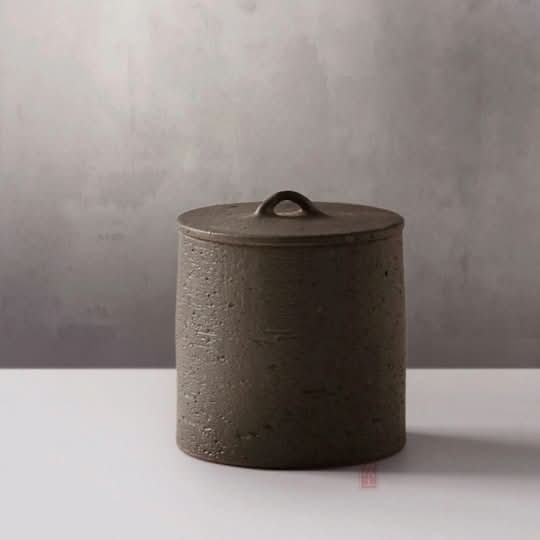 Japanese Style Raw Rustic Tea Jar: Dark gray ceramic storage jar with looped lid on white surface.