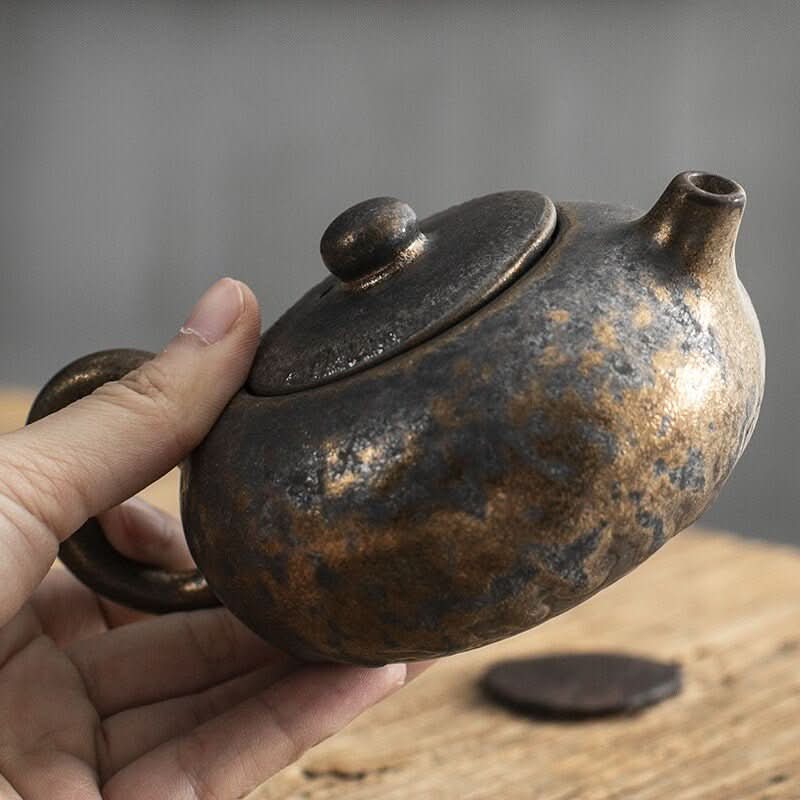 Japanese Style Stoneware Gilt Glazed Teapot with textured finish, held by hand.