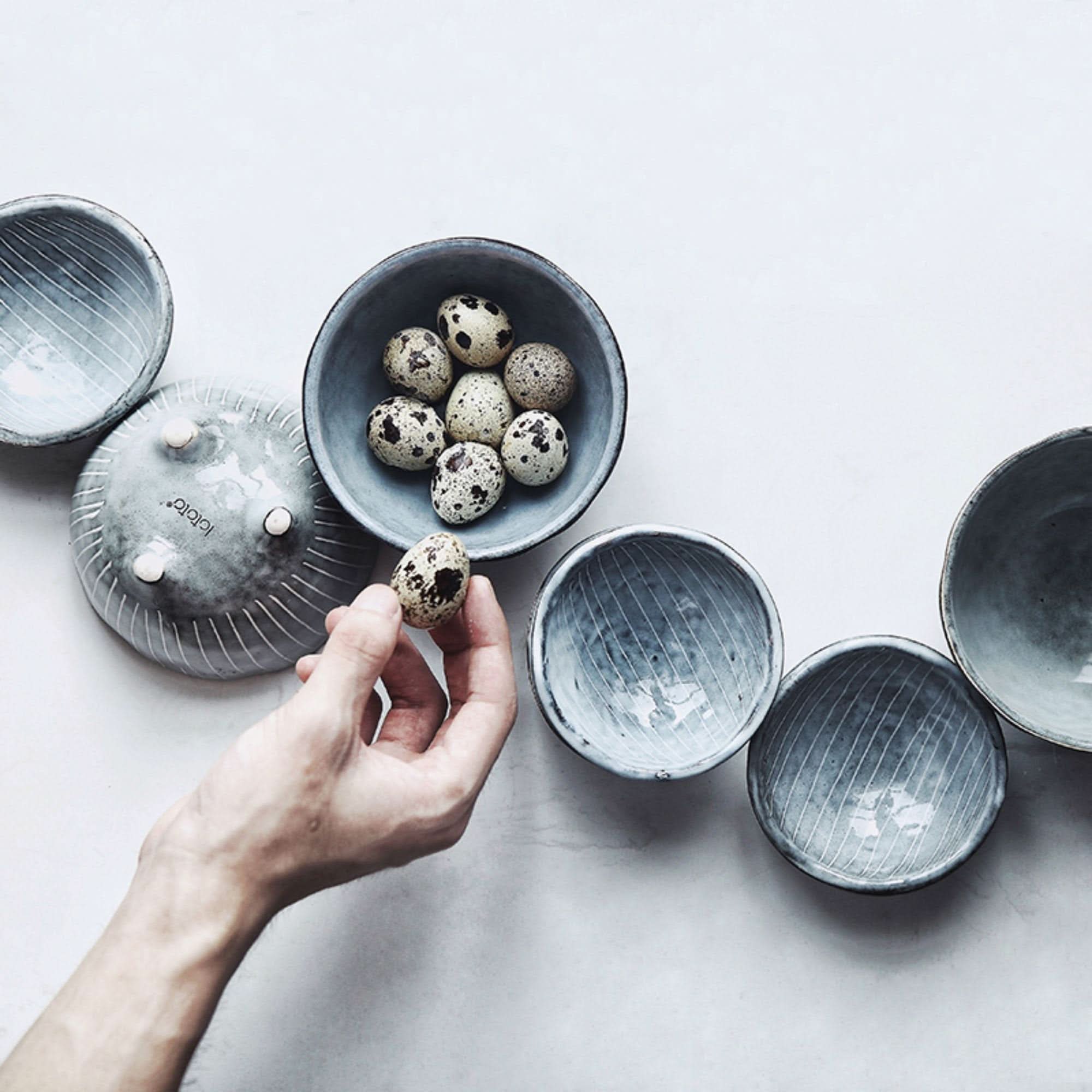 Gray ceramic Japanese tableware set with a hand holding a quail egg.
