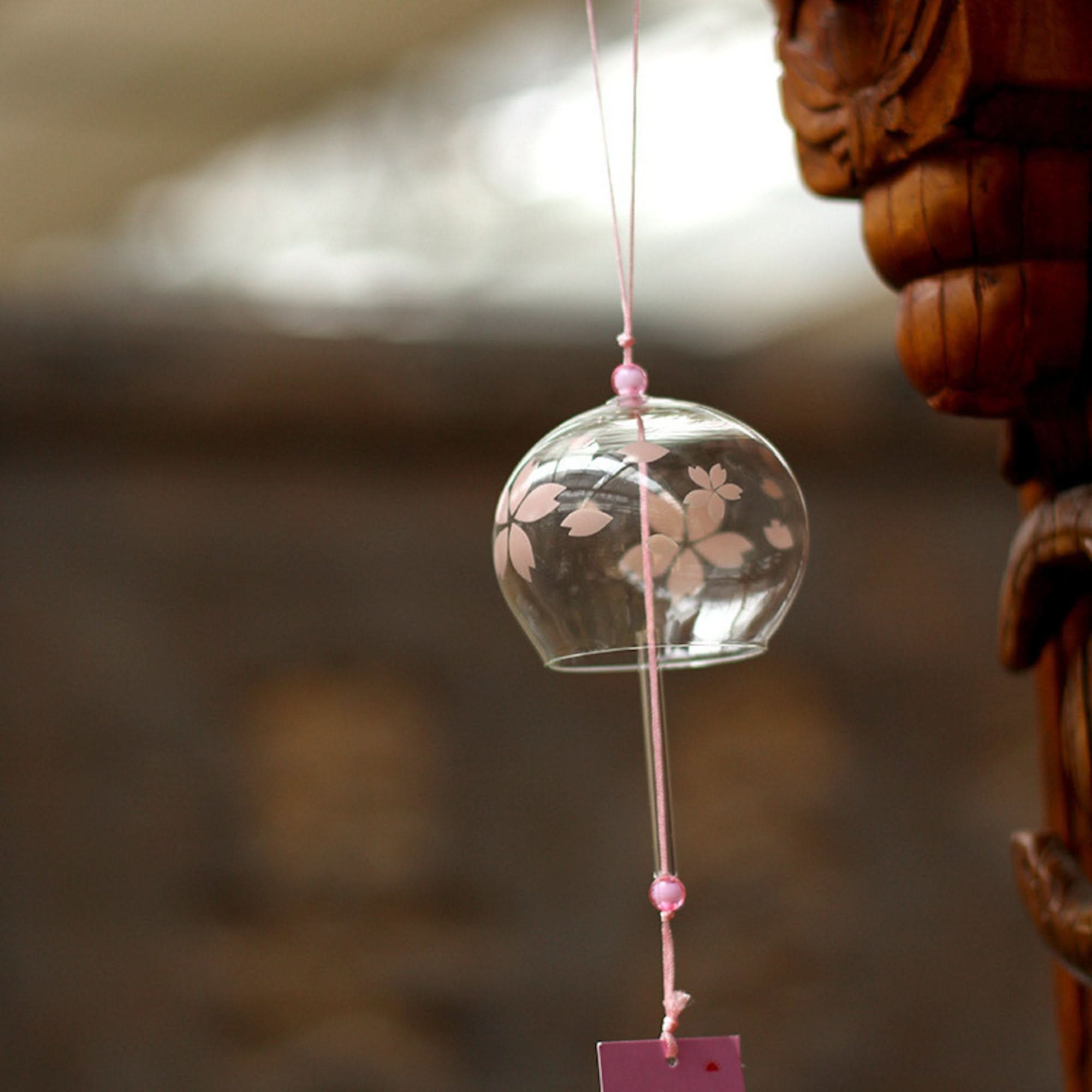 Glass Japanese wind chime with pink cherry blossoms, hanging outdoors.