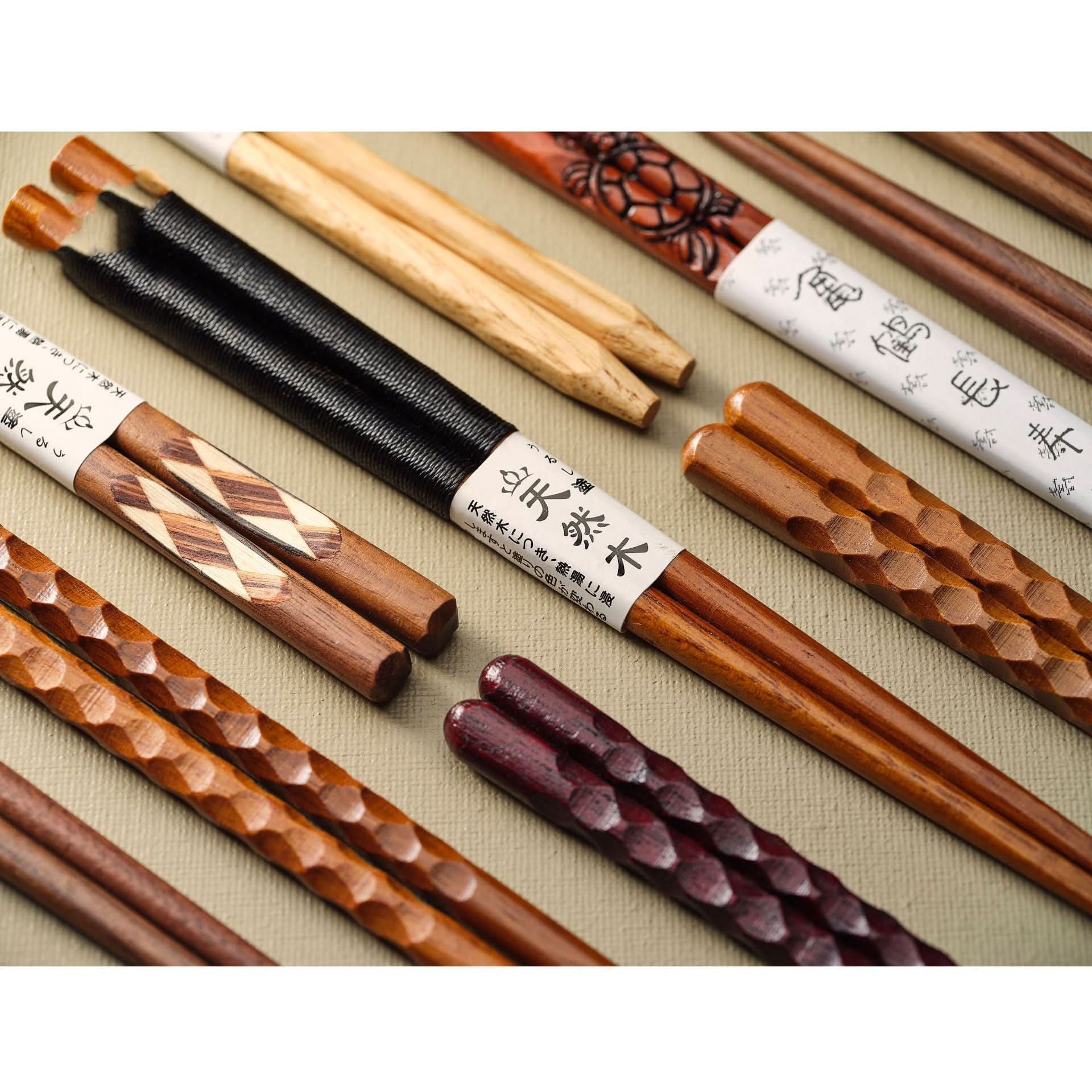 Assortment of Japanese wooden chopsticks with carvings & colors, includes spoons & rests.