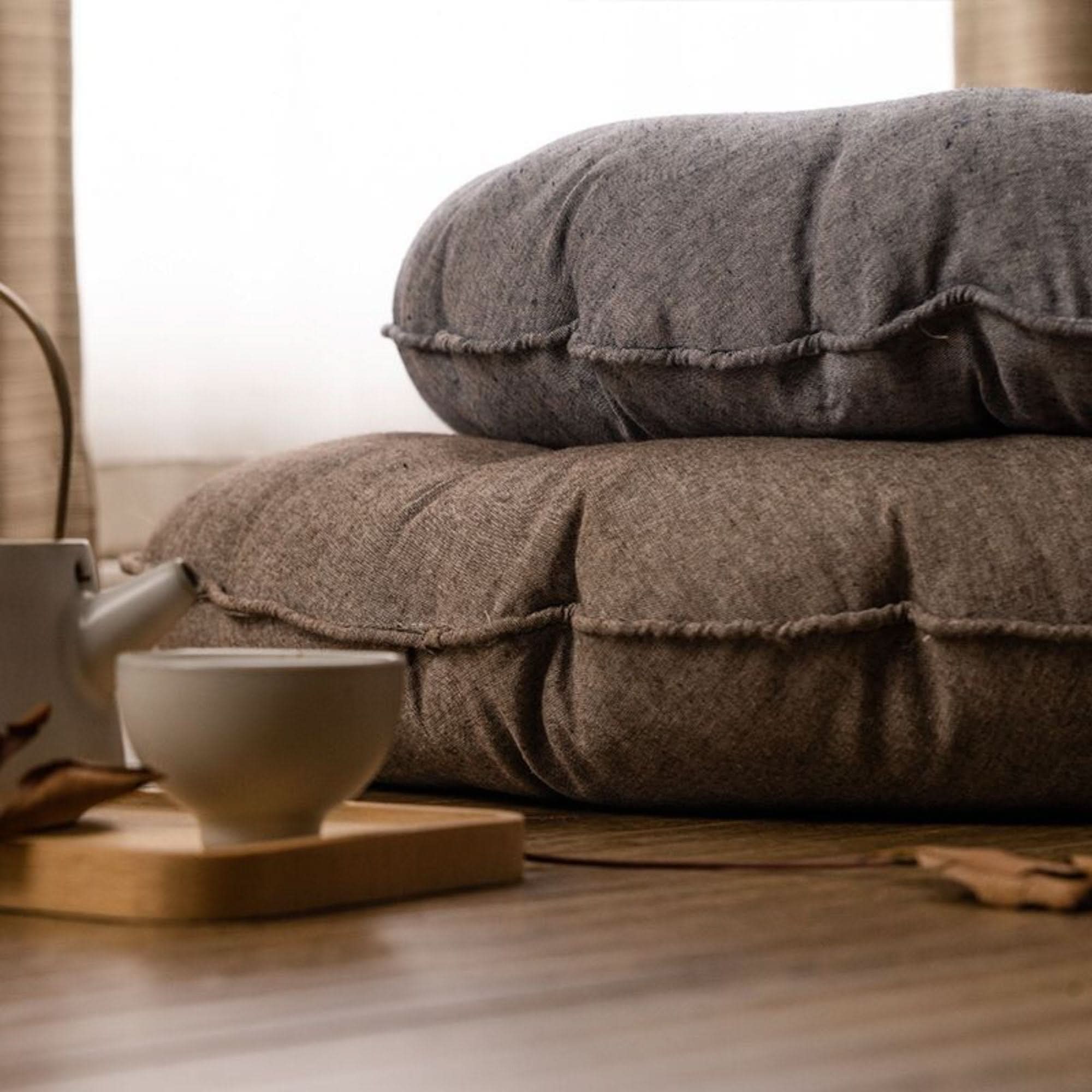 Stack of round grey and brown linen meditation cushions with frayed edges, peaceful home decor.