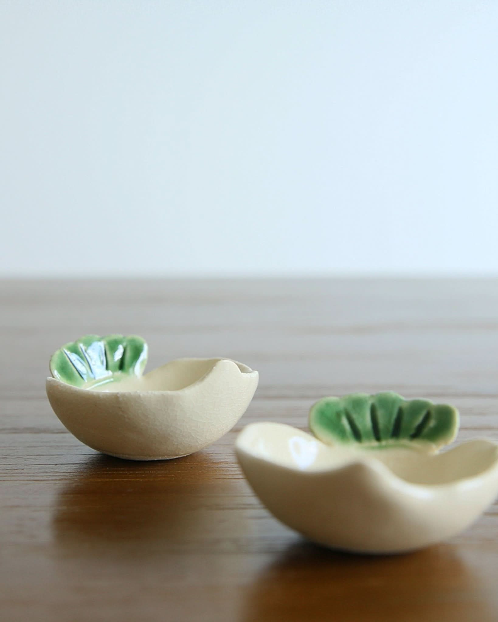 Mino-yaki handmade stoneware dip bowls with green vegetable leaf detail on wooden table.