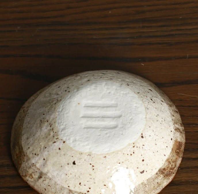 Minoyaki irregular ceramic soup bowl in off-white with speckled brown accents on wooden table.