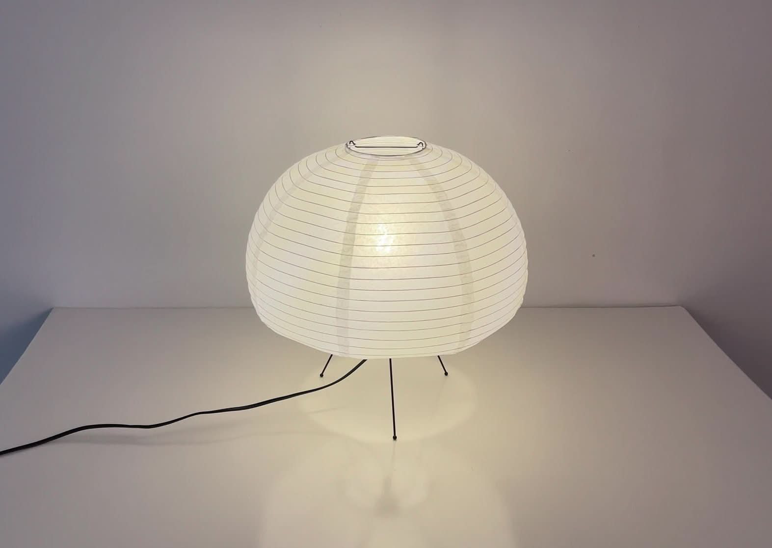 Mushroom shape paper table lamp in white on a clean white surface with a black cord.