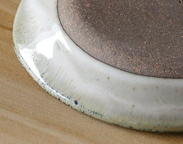 Nishida Muyu oval deep plate: White & brown speckled ceramic tableware on wood.