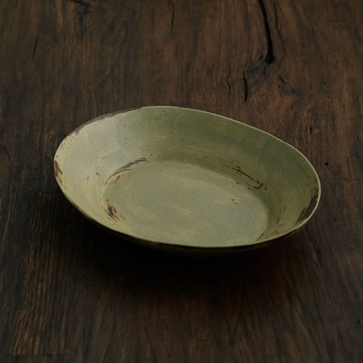 Handmade oval pottery dish, light green with rustic texture.