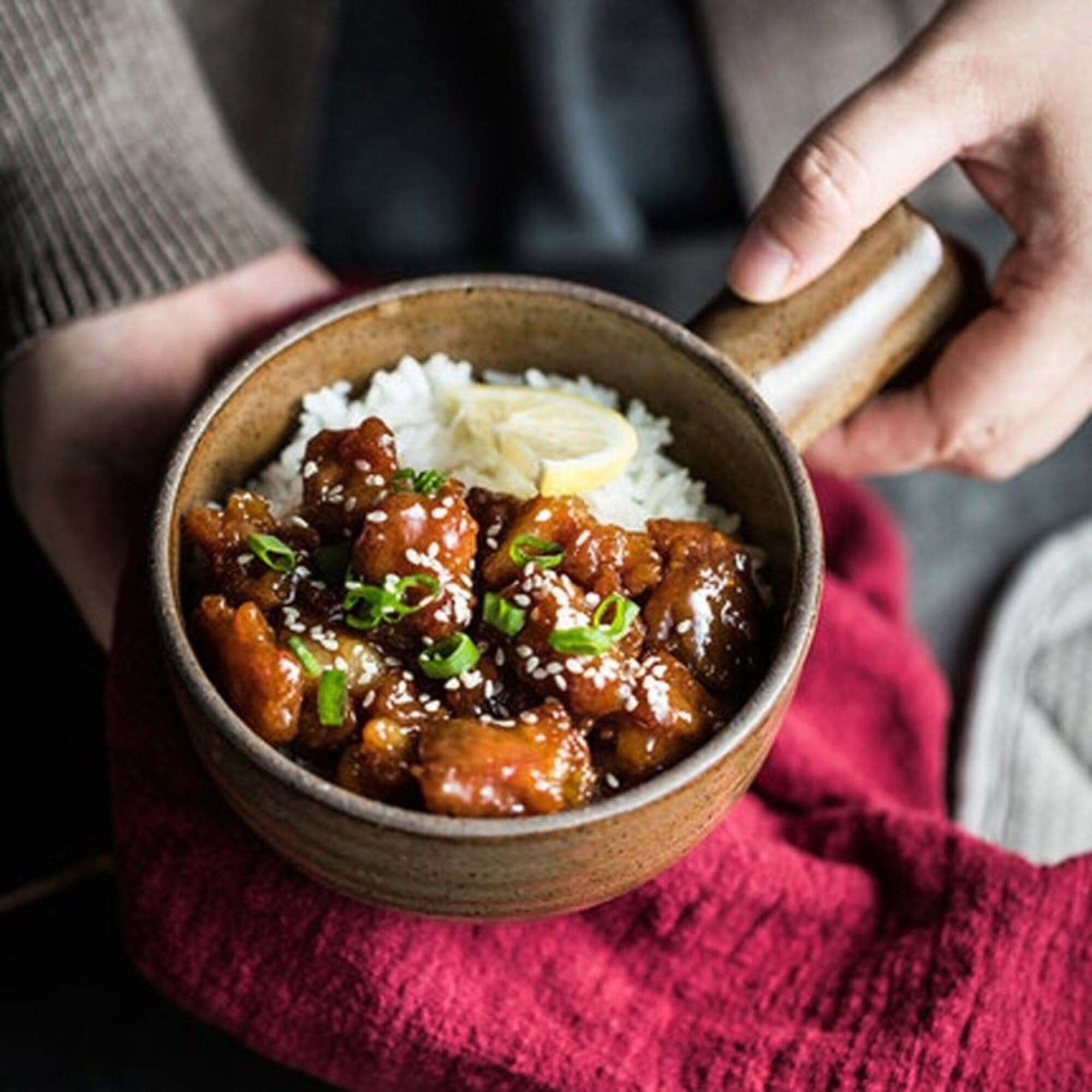 Rustic Nordic stoneware baking plate holds glazed chicken and rice, garnished with sesame seeds.