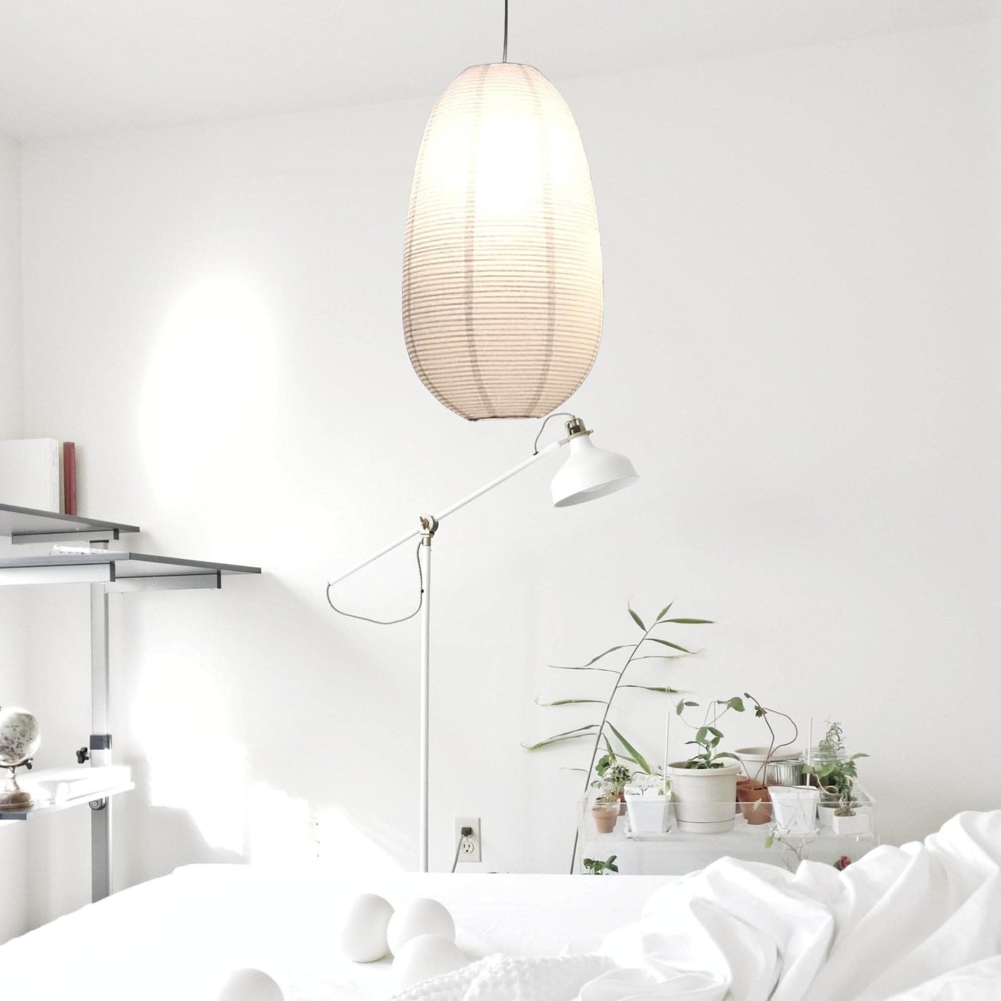 Oval paper lampshade hanging in a minimalist white room with plants and a floor lamp.