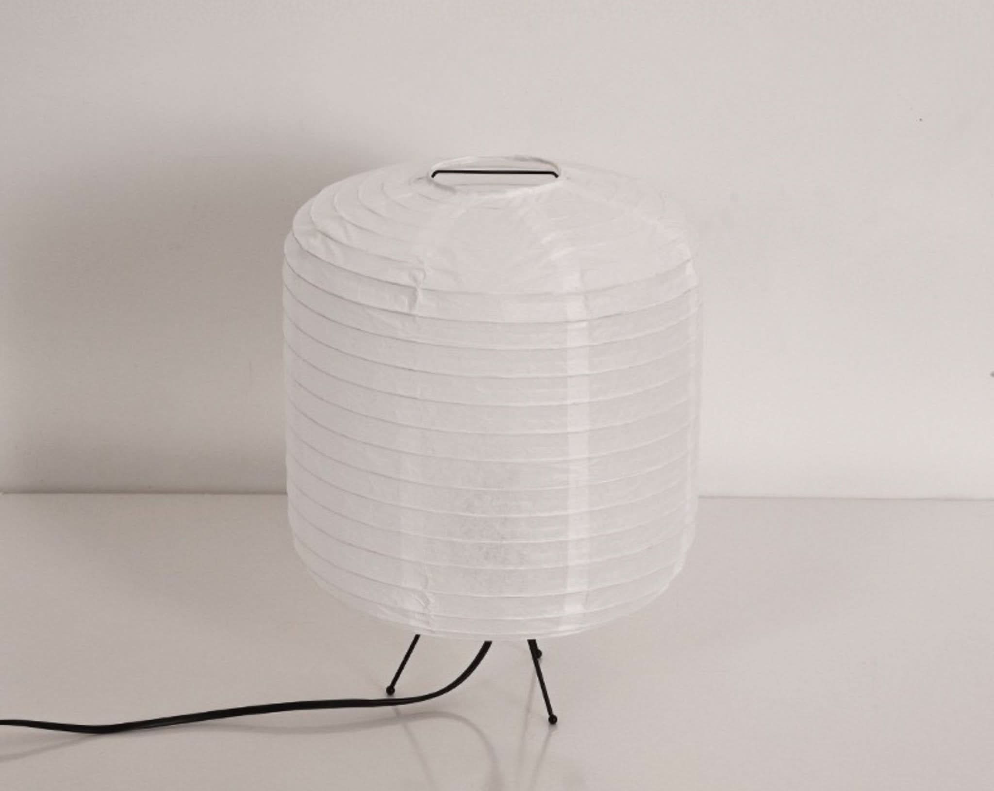 White paper table lamp with a rounded cylinder shape on black legs.