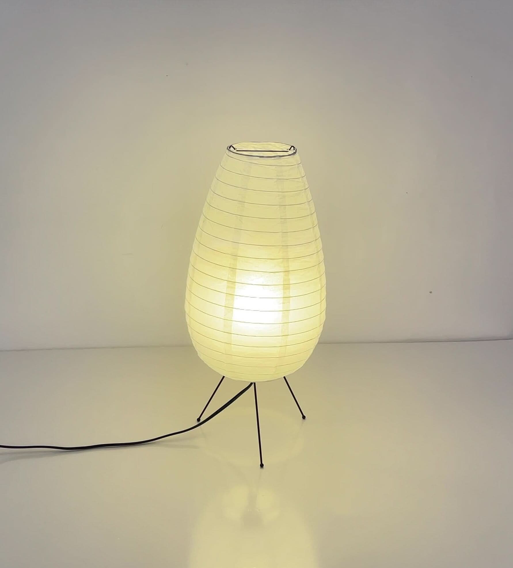 Paper Table Lamp Long Oval Lamp, a mid-century modern light with a glowing warm hue on black legs.