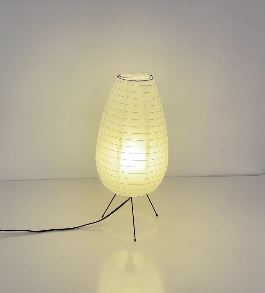 Paper Table Lamp Long Oval Lamp, a mid-century modern light with a glowing warm hue on black legs.