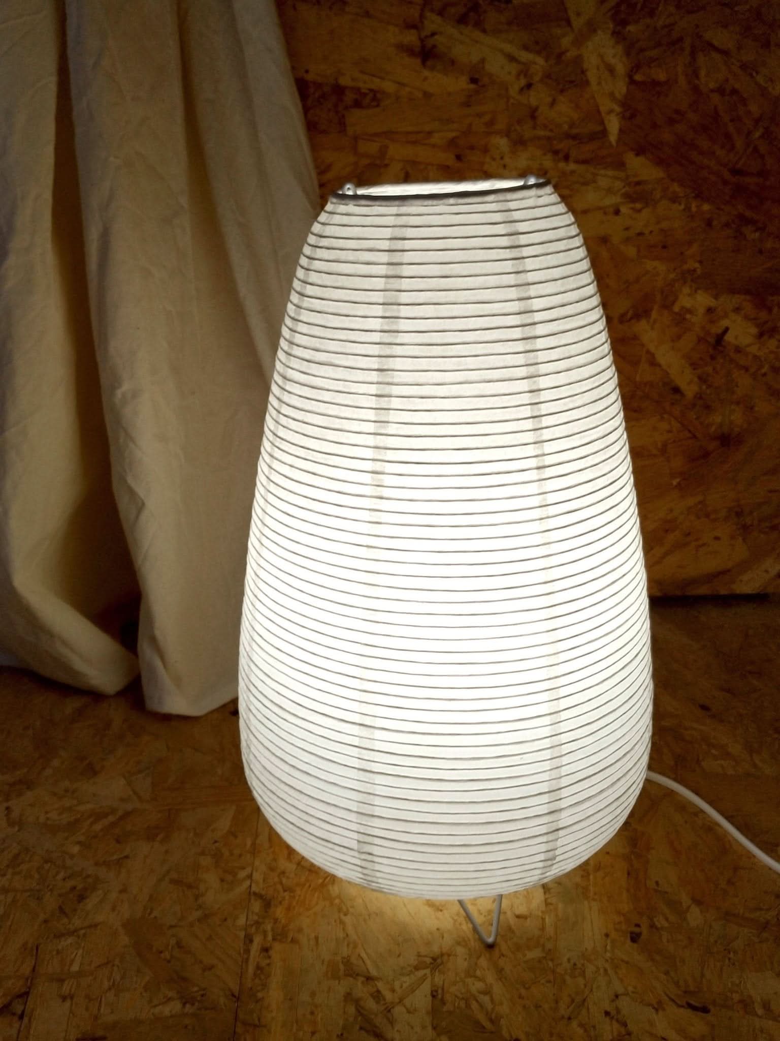 White paper table lamp elongated with black stripes on wood grain background.