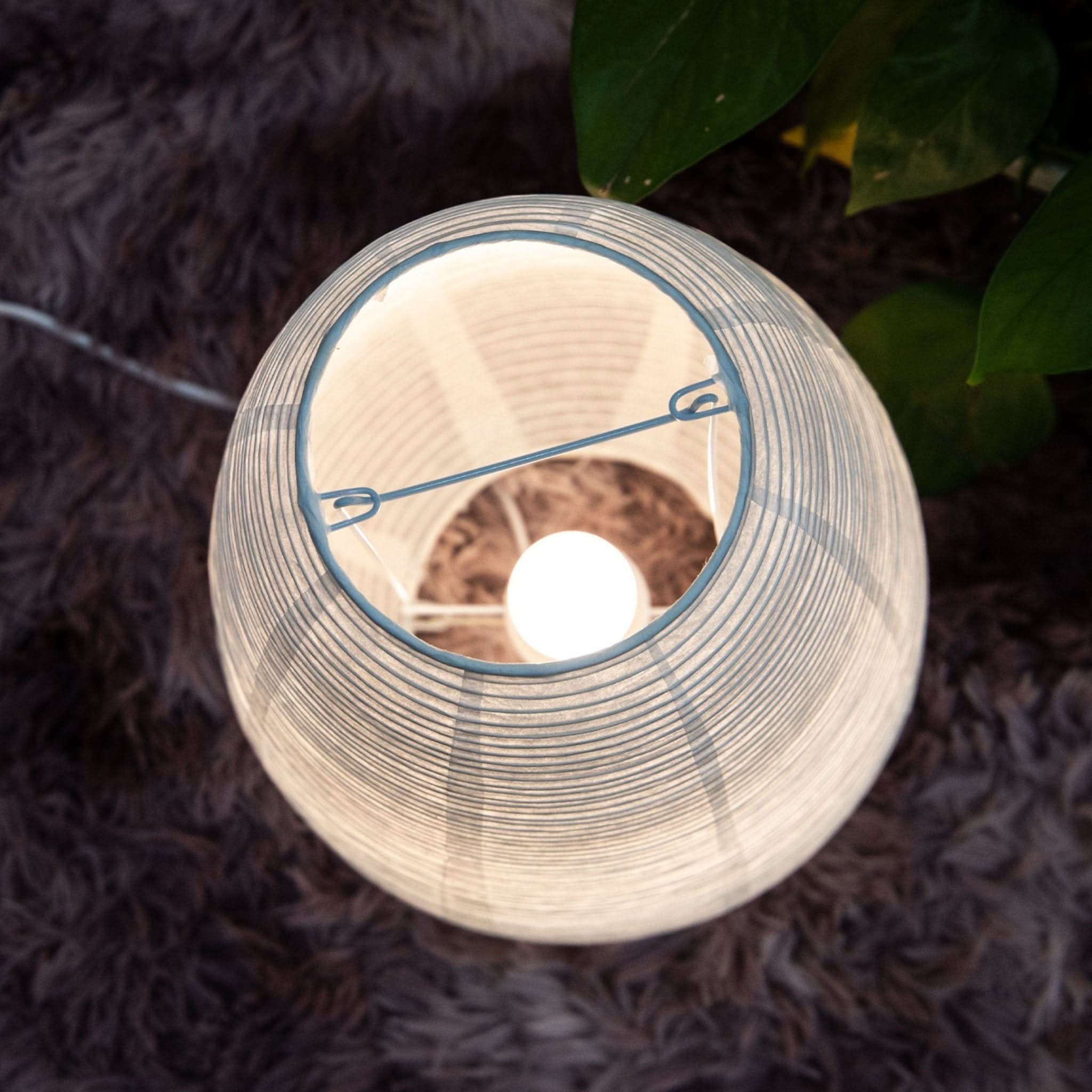 White paper table lamp, elongated shape, with blue trim on dark fuzzy rug.