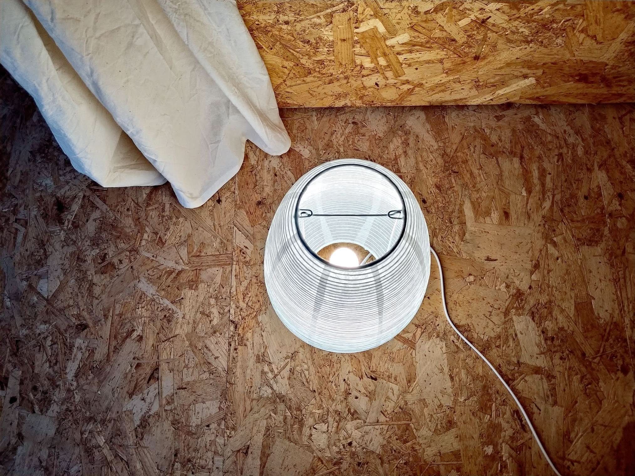 Paper Table Lamp Elongated, white ribbed paper shade illuminated on textured wood background.