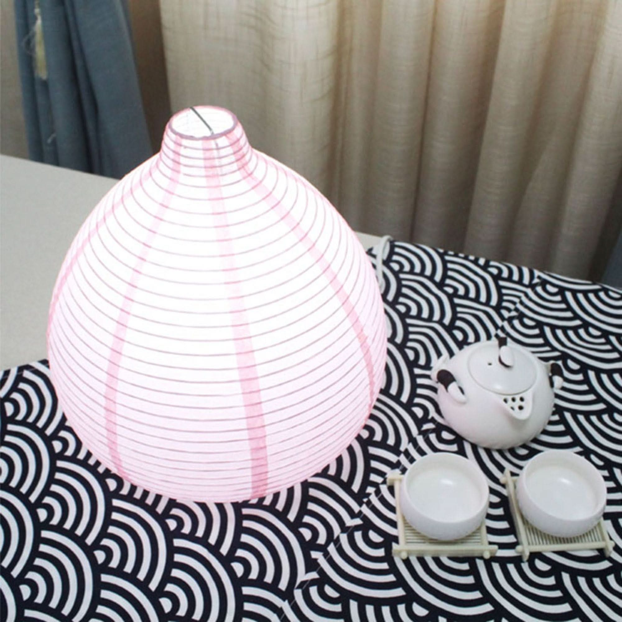 Pink paper table lamp with tear shape on a black and white wave pattern, with tea set.