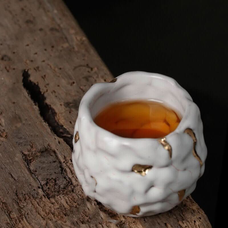 White & gold glazed Kintsugi tea cup, handmade in Japan, on rustic wood.