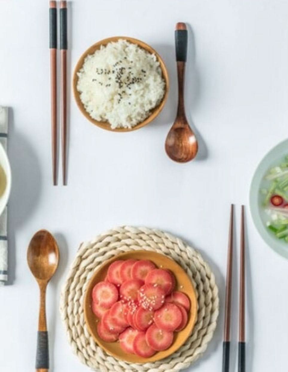 Natural wooden spoon set, chopsticks, and rest with rice and sliced carrots.