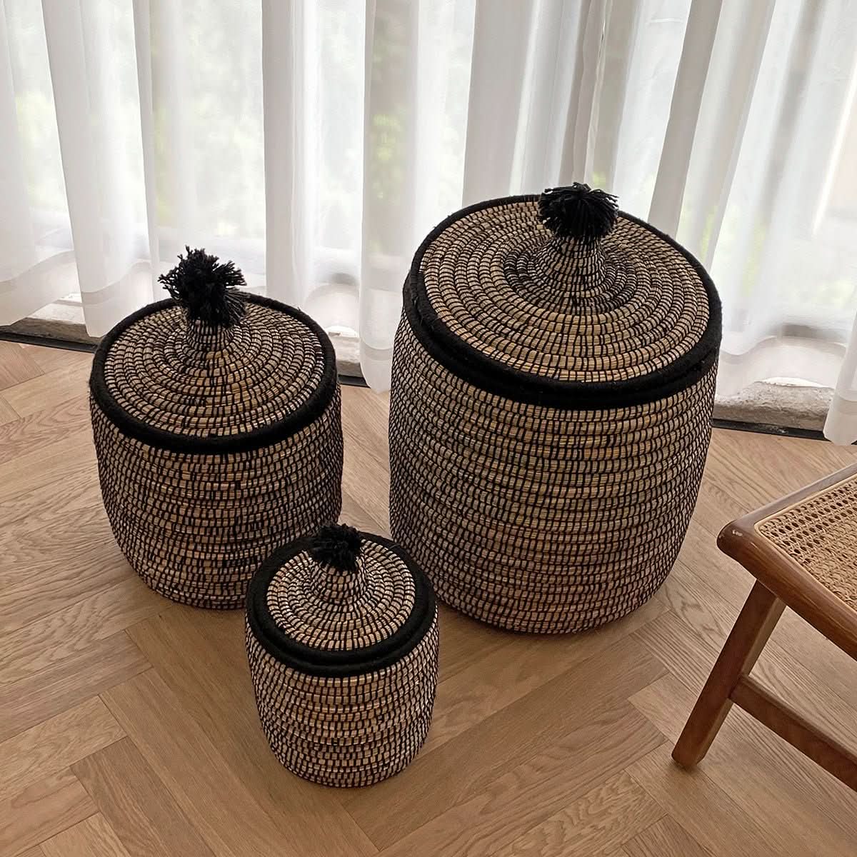 Raffia wool woven storage baskets with black trim & pom-poms, perfect for dirty laundry.