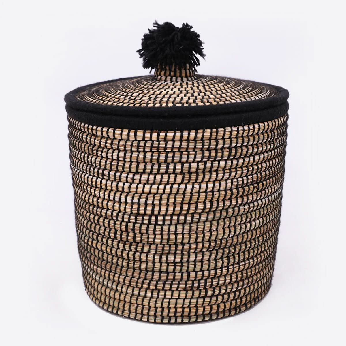Raffia wool woven storage basket with black trim and pompom lid for dirty laundry.