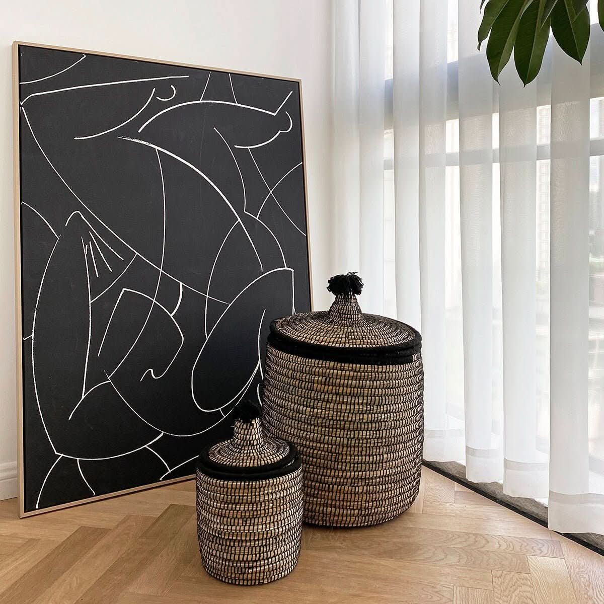 Woven rattan baskets with lids and wool tassels, home decor accents by a black & white abstract art piece.
