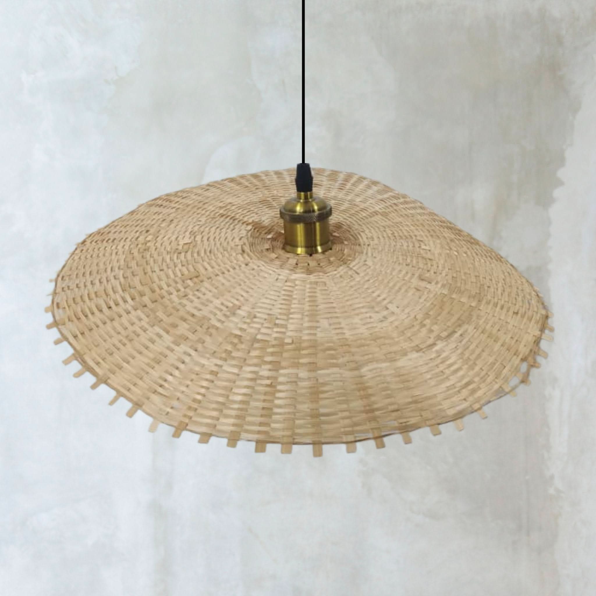 Woven natural rattan lamp shade with hat shape, brass fitting, white textured background.