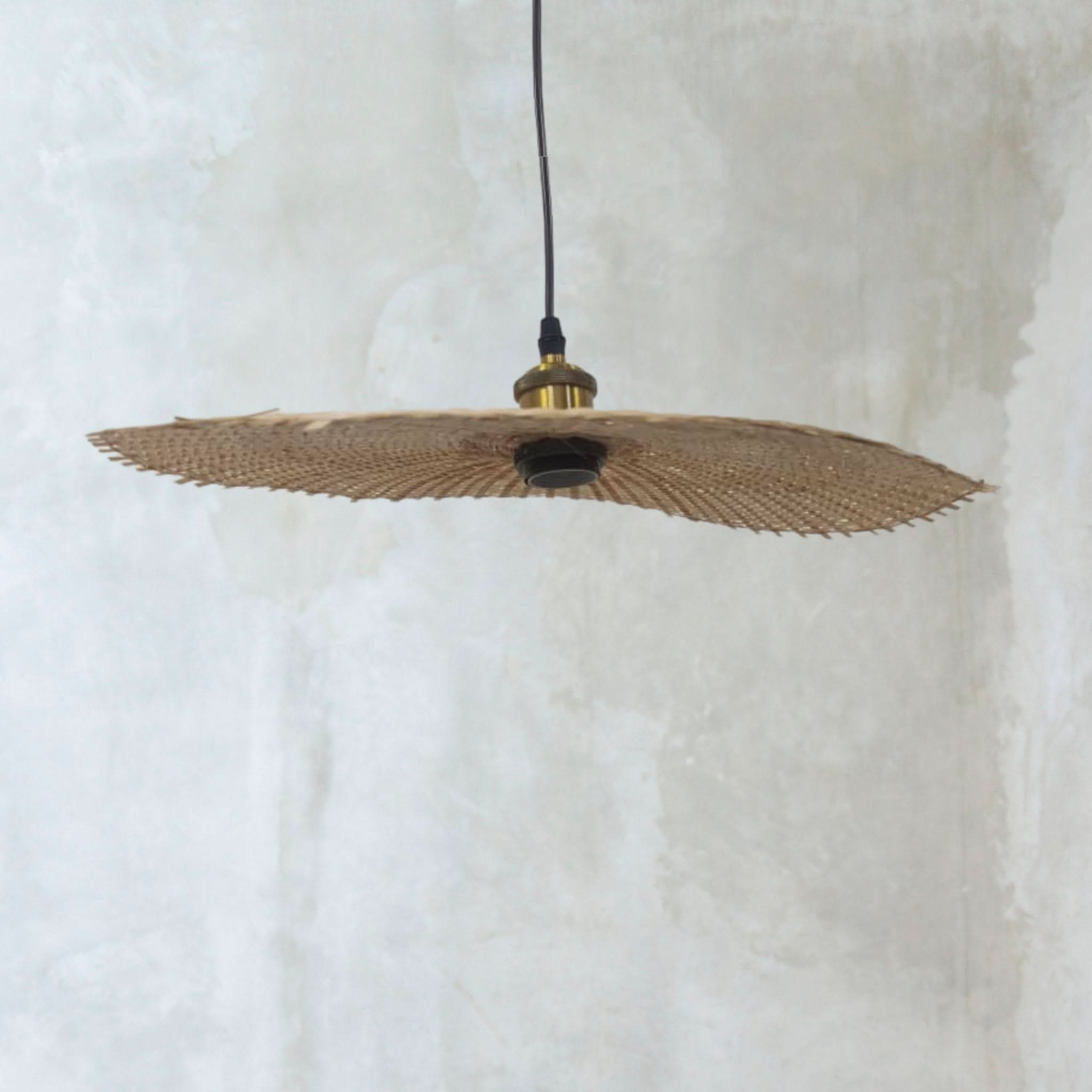 Natural rattan lamp shade with hat shape, hanging against a textured light background.