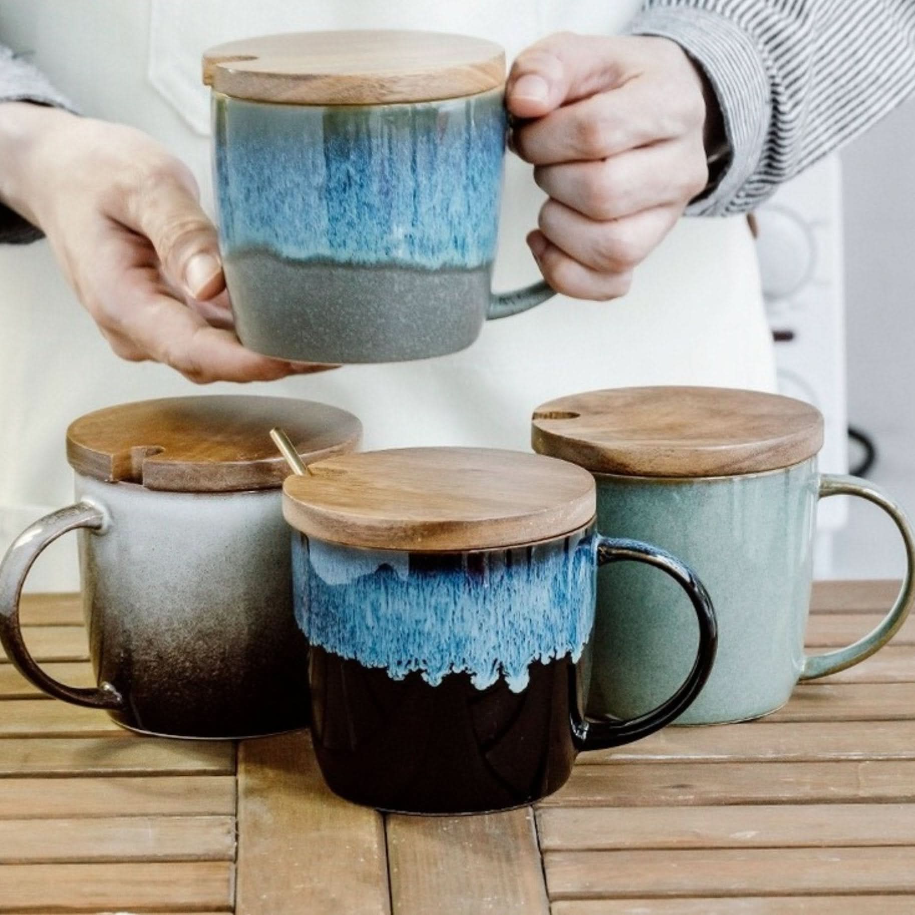 Reactive glazed ceramic mugs with wooden lids in blue, green, and ombre tones on a wooden surface.