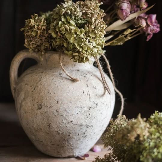 Aged texture light gray clay pot with ears, filled with dried green and pink flowers.