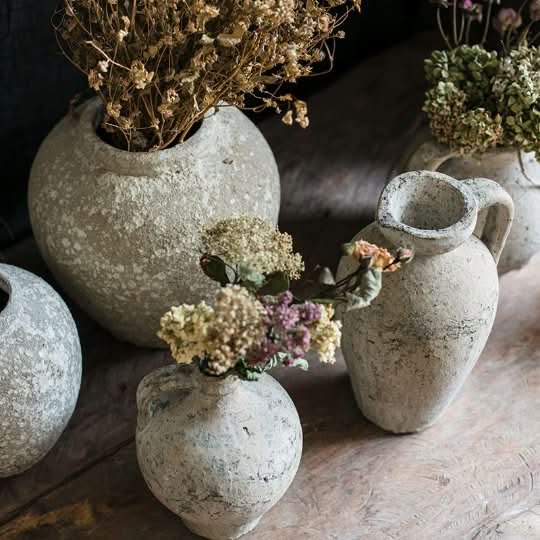 Red clay pots with ears, featuring textured grey finish and dried floral arrangements, styled on a rustic surface.