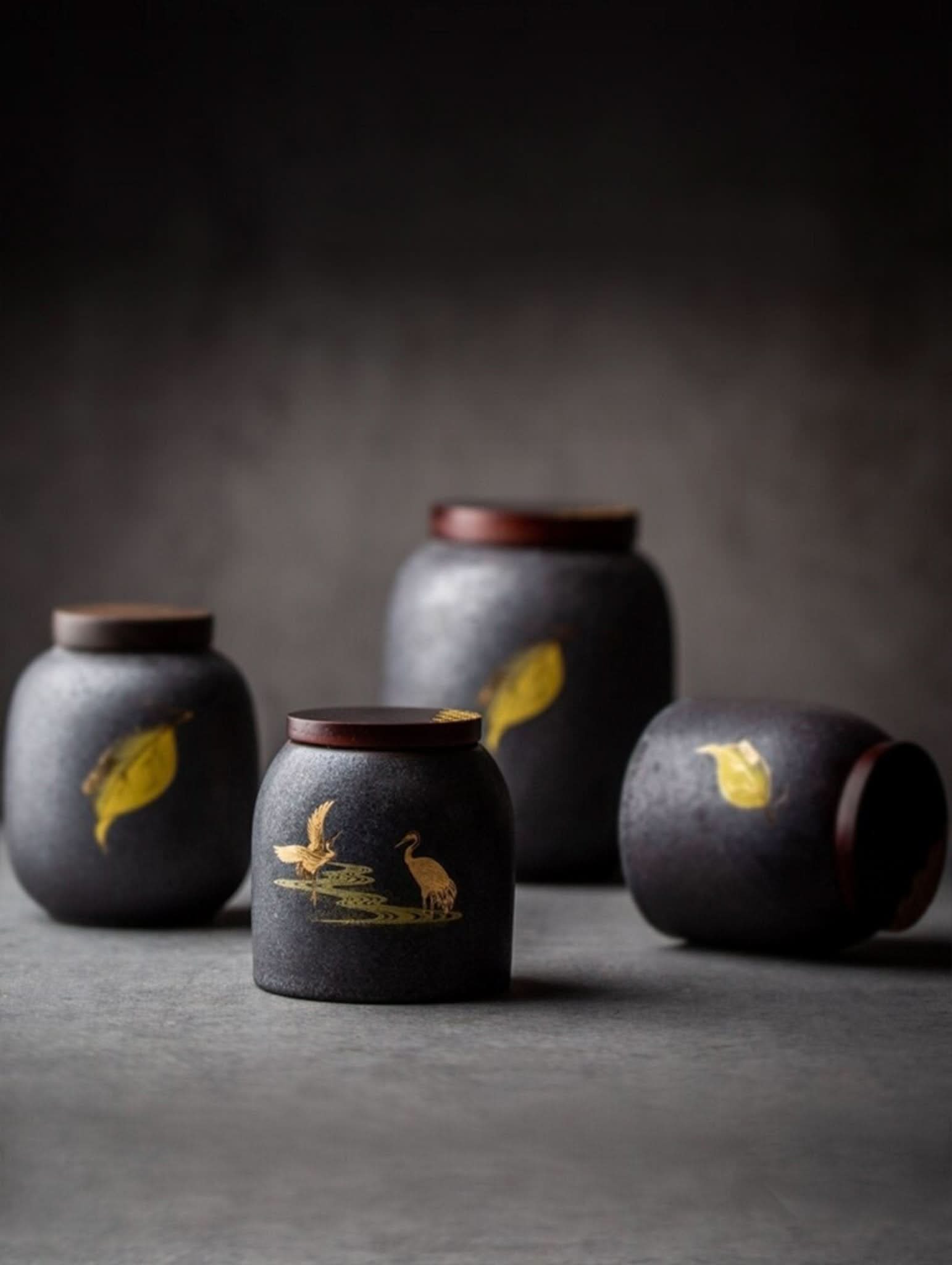 Retro black ceramic tea canisters with gold leaf and crane designs, wooden lids.