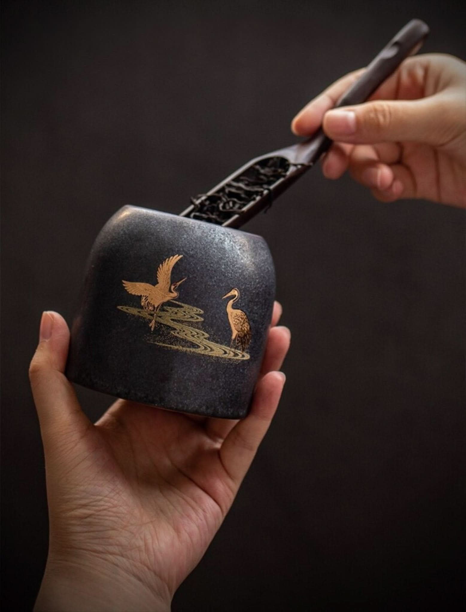 Retro black ceramic tea canister with gold cranes, filled with loose leaf tea.