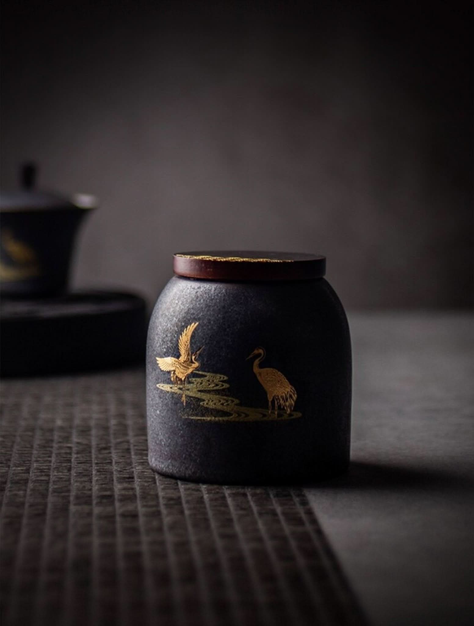 Retro black ceramic tea canister with gold crane design on textured surface.