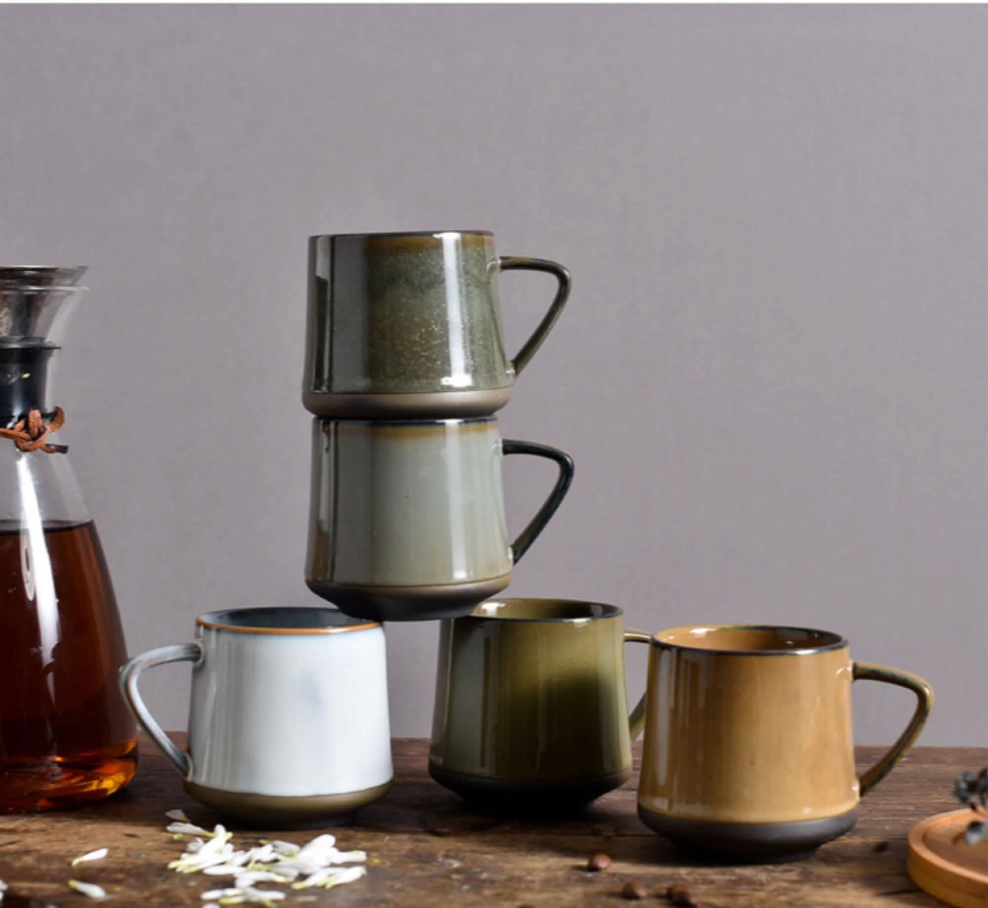 Stack of glazed ceramic mugs in earthy tones: white, olive green, and tan. Home Decor.