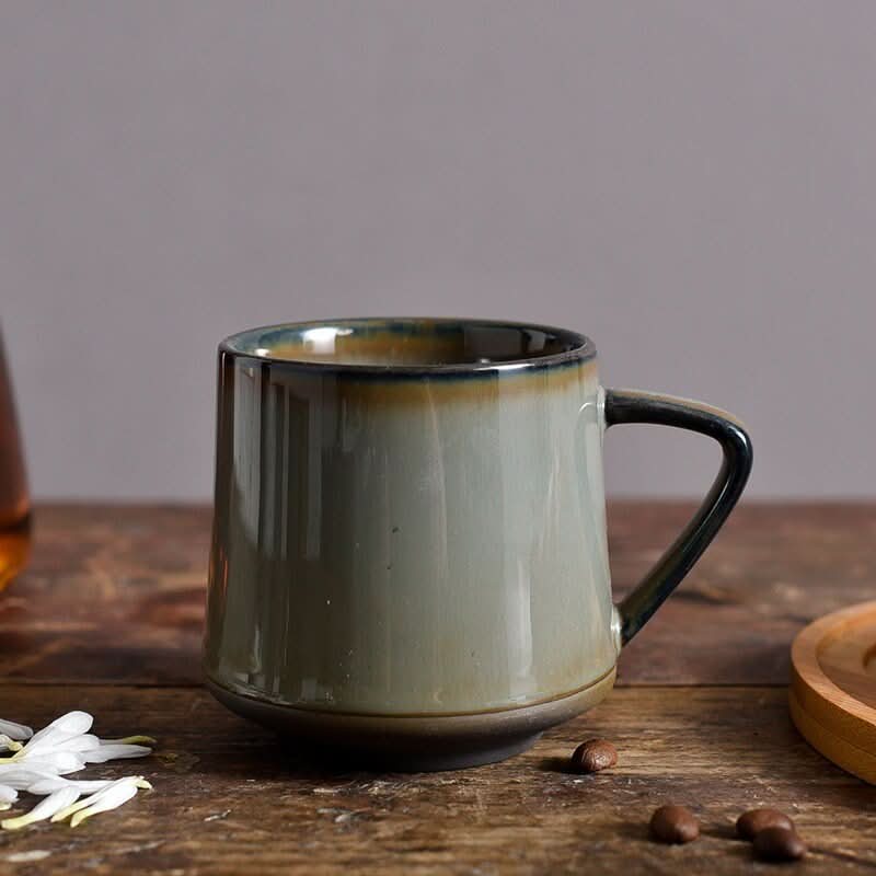 Glazed ceramic mug in sage green with ombre rim, on rustic wood surface.