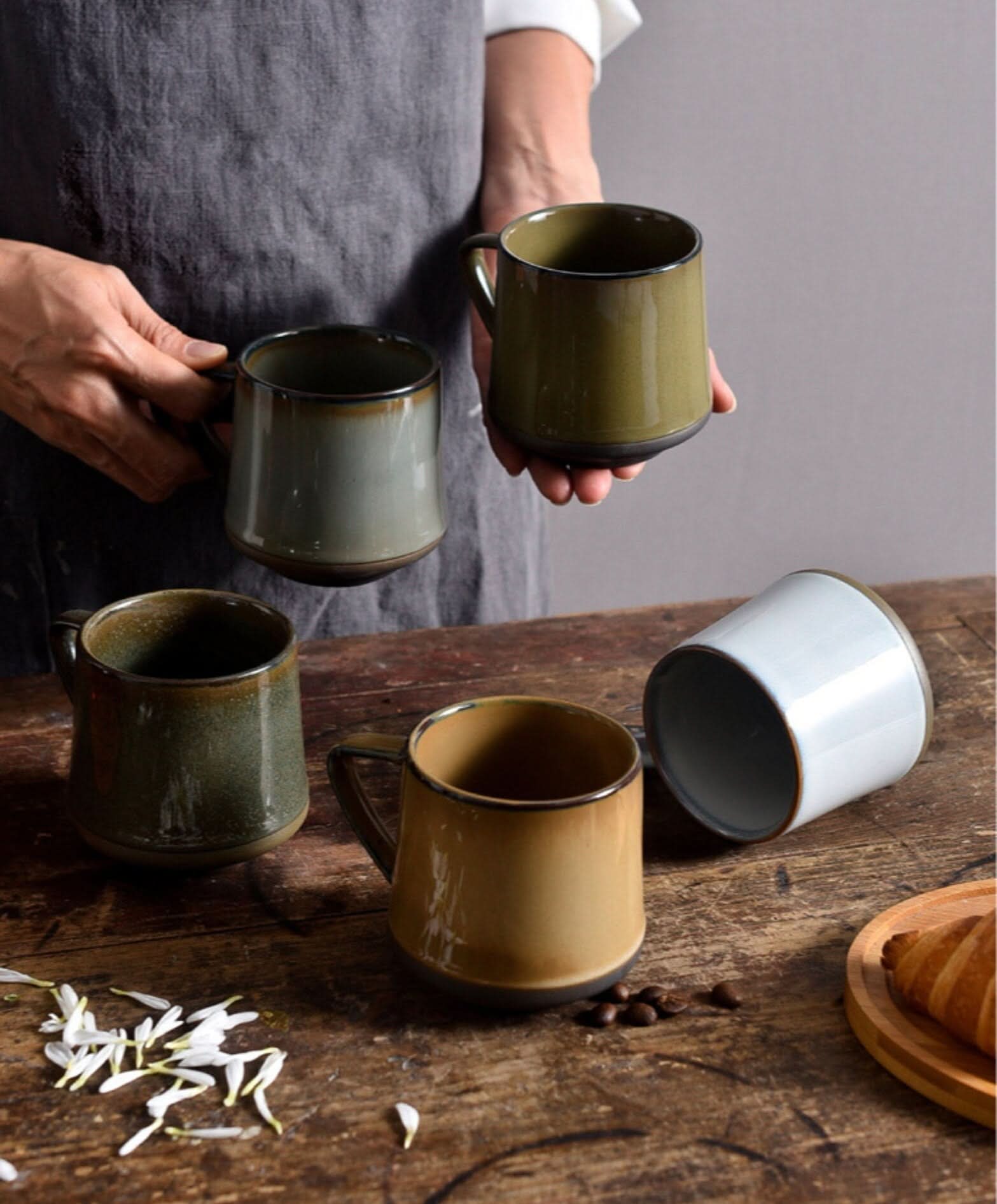Assorted glazed ceramic mugs in green, tan, and blue hues on a rustic wooden table.