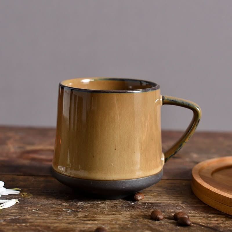 Rustic glazed ceramic mug in amber and dark grey, coffee beans and wooden saucer on rustic table.