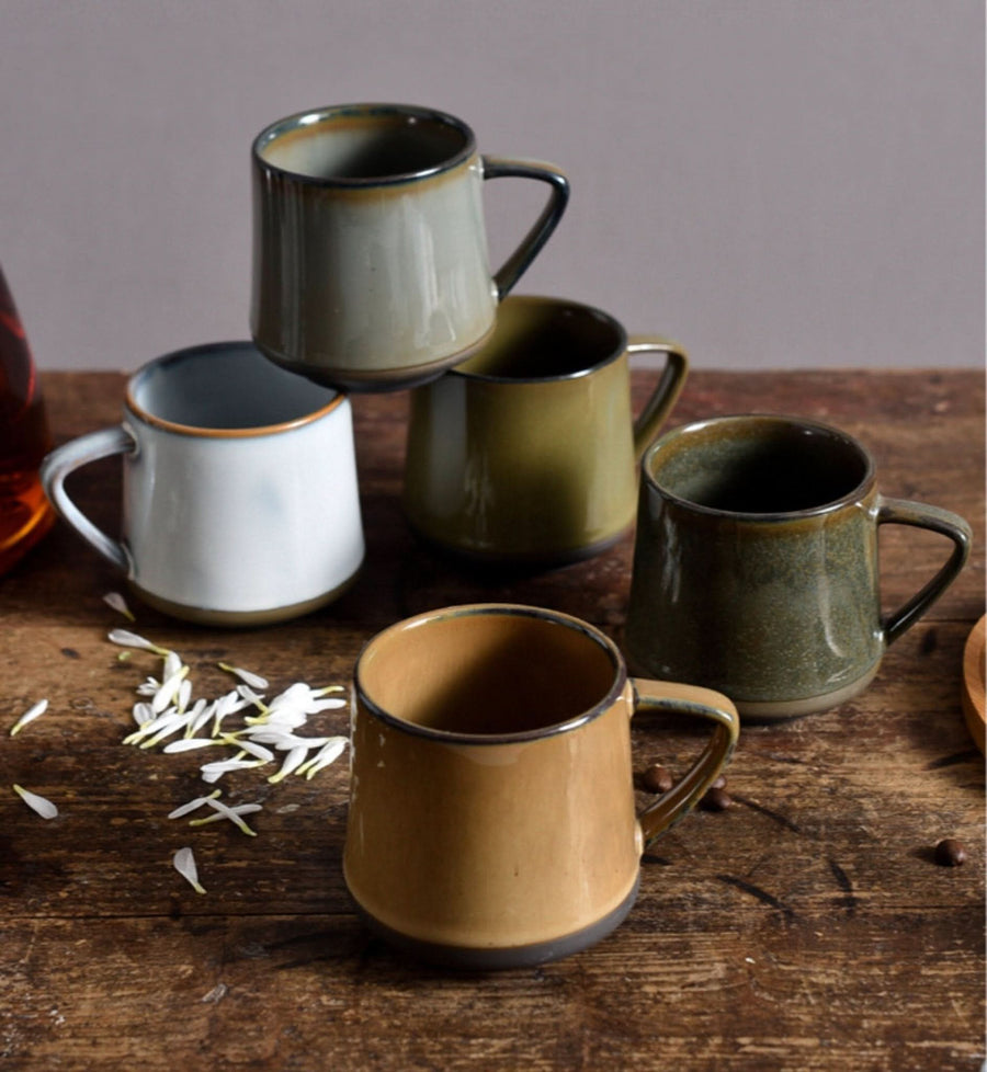 Assortment of glazed ceramic mugs in earthy tones on a rustic wooden table.