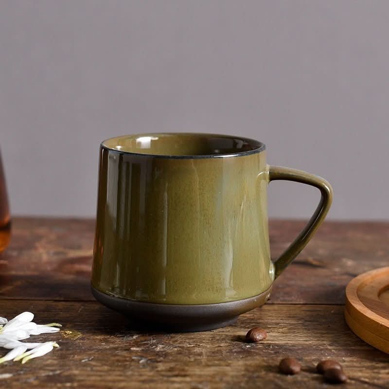 Olive green glazed ceramic mug on rustic wooden table with coffee beans and white flowers.