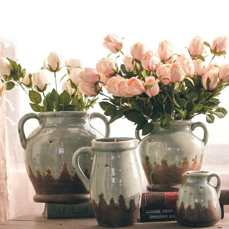 Retro distressed gray-blue binaural ceramic vases with pink roses on a dining table.