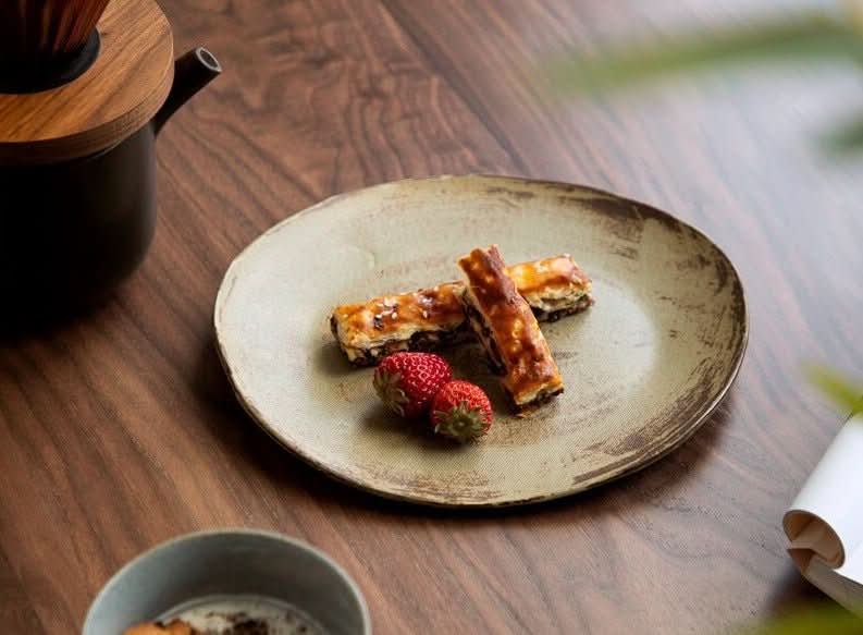 Rustic brown irregular flat plate, hand-made, holding pastries and strawberries.