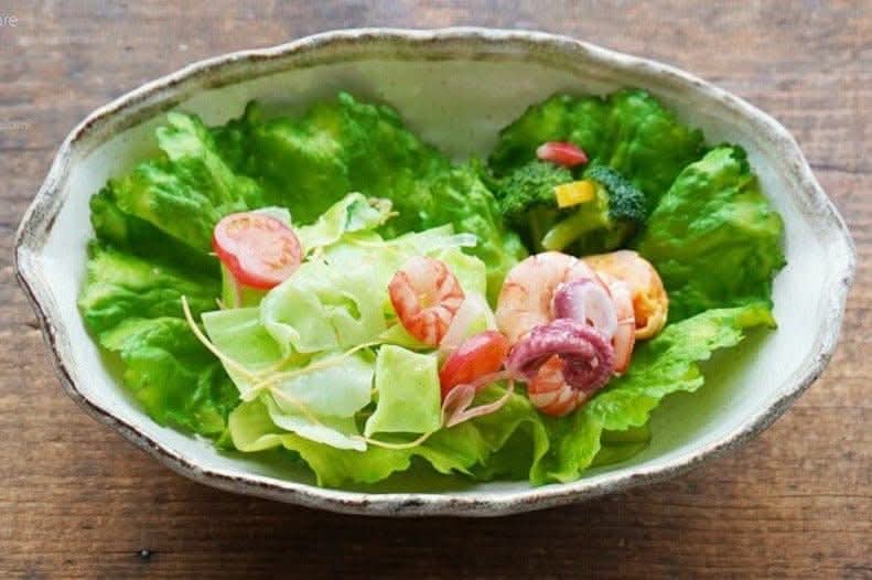 Rough pottery stoneware bowl holding fresh salad with shrimp and octopus.