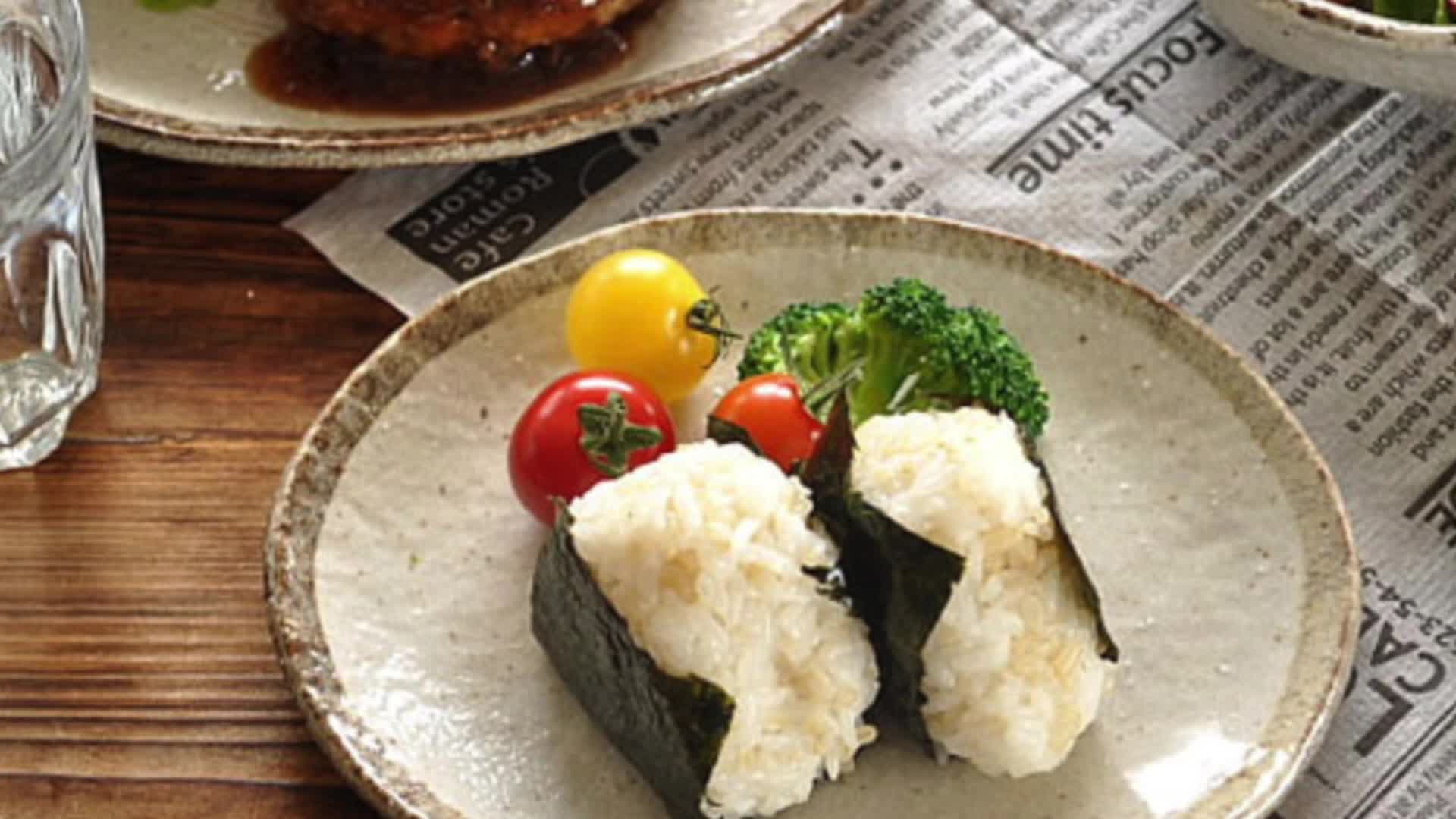 Rough pottery stoneware dinner set holds onigiri, tomatoes, and broccoli on newspaper.