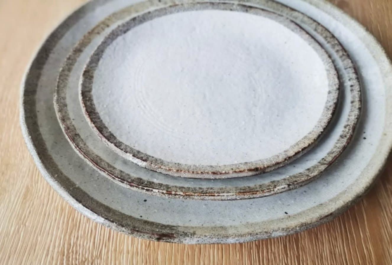 Rough pottery stoneware dinner set with textured white centers and earthy brown rims on a wooden surface.
