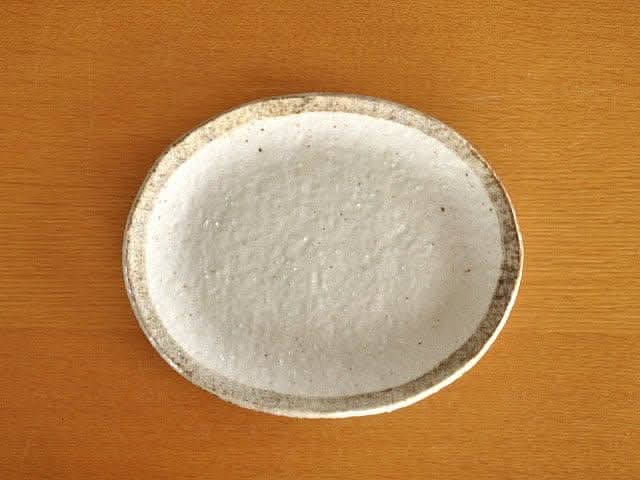 Rough pottery stoneware dinner set plate, white ceramic with speckled brown rim on wood grain table.