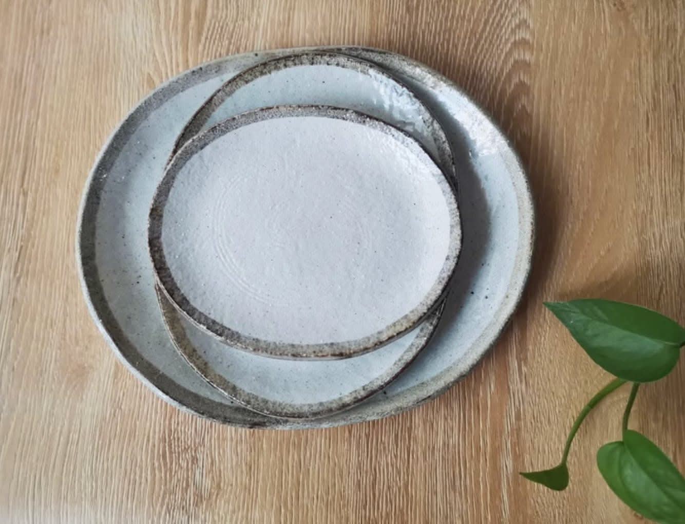 Rough pottery stoneware dinner set stacked on a wooden table with a green plant leaf.