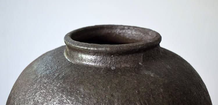 Rustic distressed rounded vase with shiny black texture and circular engraving detail.