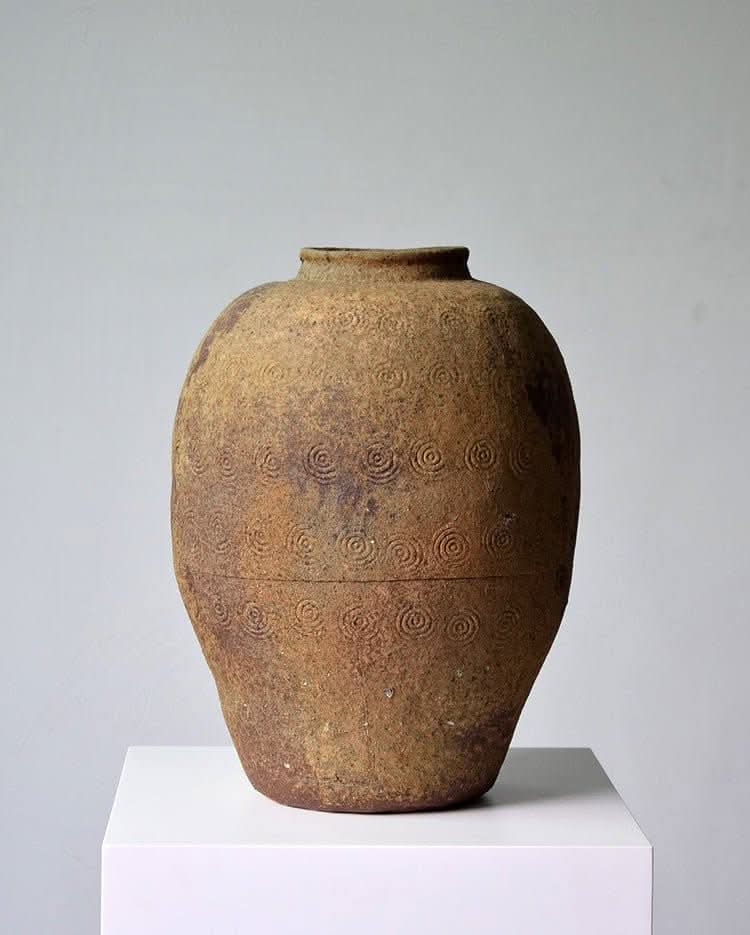 Rustic Distressed Rounded Vase with Circular Engraved Pattern, dark green blue glaze, on white pedestal.